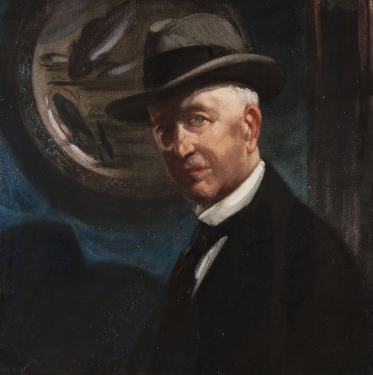Portrait of a man with silver hair and blue eyes, wearing a dark hat and dark suit.